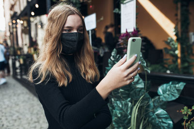 Young woman having video call talking while walking downtown wearing the face mask