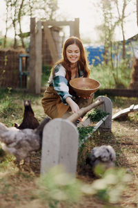 Smiling woman feeding chickens in farm