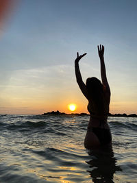 Silhouette woman with arms raised at beach against sky during sunset