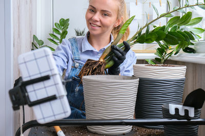 Gardener woman blogger using phone while transplants indoor plants and use a shovel on table. 