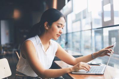 Young woman using phone while sitting on table