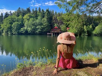 Rear view of  woman wearing pink dress and hat sitting down and looking at the lake in summer