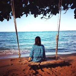 Rear view of woman sitting on beach against clear sky