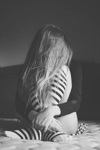 Depressed woman with messy hair hugging knees while sitting on bed at home