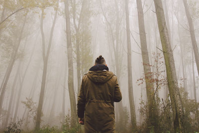 Rear view of man standing in forest during foggy weather