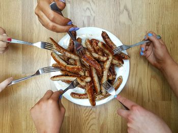 Cropped image of friends eating sausages in plate on table