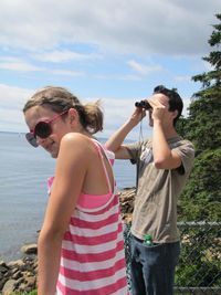 Man with woman looking through binoculars at beach against sky