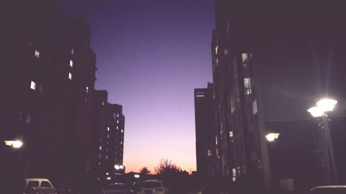 Illuminated street amidst buildings against sky at night