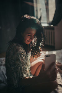 Young woman using smart phone while sitting on laptop