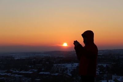 Silhouette man using mobile phone while standing on mountain against sky at sunset