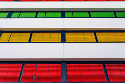 Elevation of a modern office building with different colors of blinds on each floor.