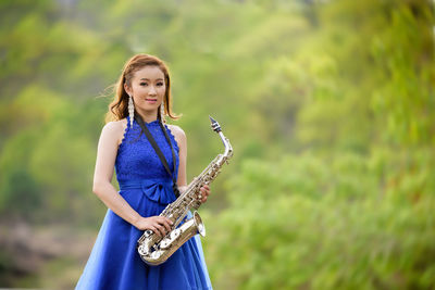 Portrait of smiling young woman with saxophone standing against plants
