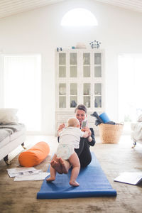 Happy mother playing with daughter while sitting on exercise mat in home office