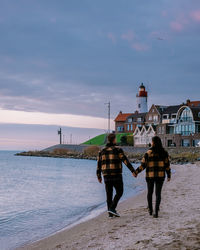 Rear view of couple walking on seashore against sky