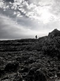 Man standing on cliff by sea against sky