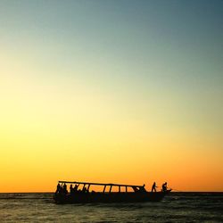 Silhouette people on boat in clear sea against orange sky during sunset