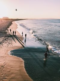 High angle view of people enjoying at beach against sky during sunset