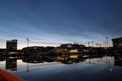 Illuminated buildings by lake against sky during sunset