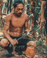 Shirtless man chopping coconut with machete