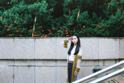 Portrait of woman standing by railing against trees