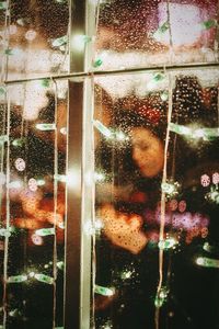 People seen through wet window with illuminated christmas lights at night