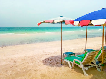 Deck chairs and parasols on beach against sky