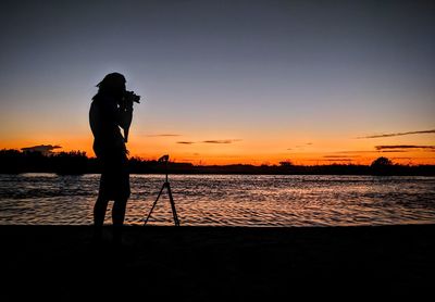 Silhouette man photographing sea against sky during sunset