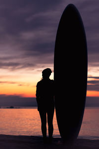 Silhouette of a woman and a surfboard on the coastline during colorful sunrise