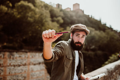 Man holding pencil and book while sitting outdoors