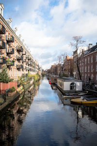 Boats moored in canal amidst buildings in city against sky