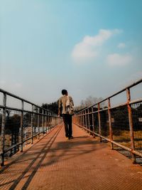 Rear view of man on footbridge against sky