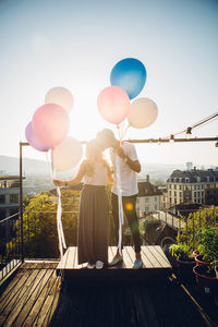 Couple standing with balloons against sky