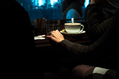 Midsection of woman with coffee cup on table sitting in cafe