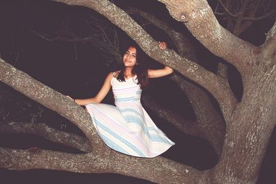 Portrait of young woman standing on tree at night