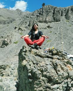 Full length of woman meditating while sitting on rock