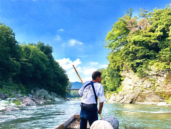 Rear view of man on rock by river against sky