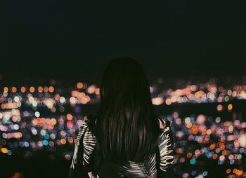 Rear view of woman standing at illuminated night