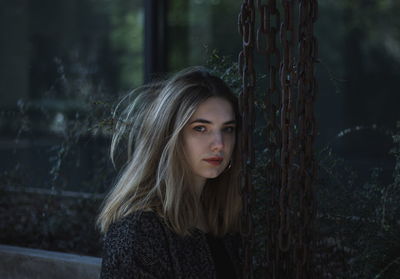 Portrait of young woman by chain against window