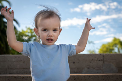 Portrait of cute boy with arms raised against sky