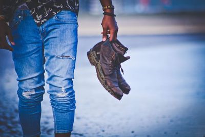 Midsection of woman holding shoes while walking on street during rainy season