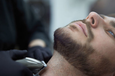 Portrait of young man who sitting in barbershop and woman hairdresser cut hair