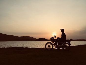 Silhouette man riding bicycle on sea against sky during sunset