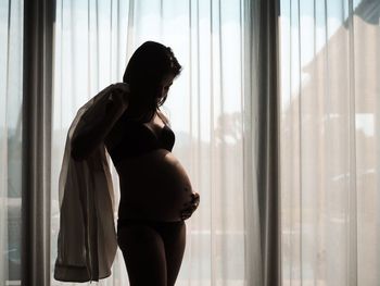 Side view of woman standing by window at home