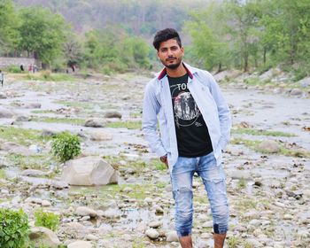 Portrait of young man with hands in pocket standing at forest