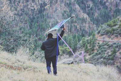 Rear view of young man holding kite while standing on grassy field