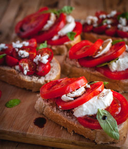 Close-up of bruschetta with cheese, tomatoes, fresh basil and balsamic vinegar on cutting board
