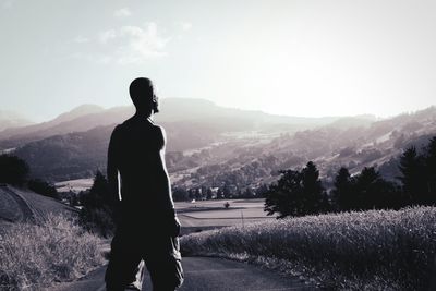 Shirtless man standing on road by mountains against sky