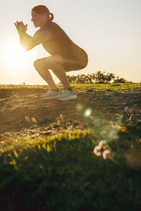 Mature woman practicing squats on grass at sunset