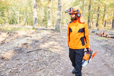 Man carrying chainsaw while walking in forest
