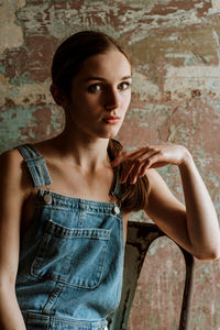 Portrait of young woman sitting on chair against wall